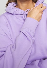 Sudadera de lavanda hecha de una suave mezcla de algodón. Presenta un cordón en el cuello y puños acanalados. Textura suave con detalles de ajuste relajado.