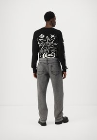 Pulover negru tricotat cu desene grafice albe pe spate, asortat cu blugi gri largi din denim și pantofi negri cu talpă groasă.