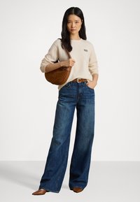 Sweater bege com bordados, jeans de perna larga azuis, cinto de couro castanho e uma bolsa castanha com formato curvo. Textura suave, design casual.