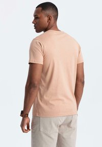 Světle růžové bavlněné tričko s kulatým výstřihem a krátkými rukávy, zobrazené ze zadní strany. Materiál má hladkou texturu a minimální švy.