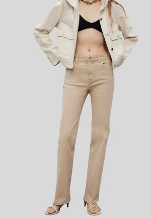 Beige High-Waist-Jeans mit geradem Bein, aus Denim; kombiniert mit einer kurz geschnittenen, cremefarbenen Jacke und einem schwarzen Oberteil darunter.