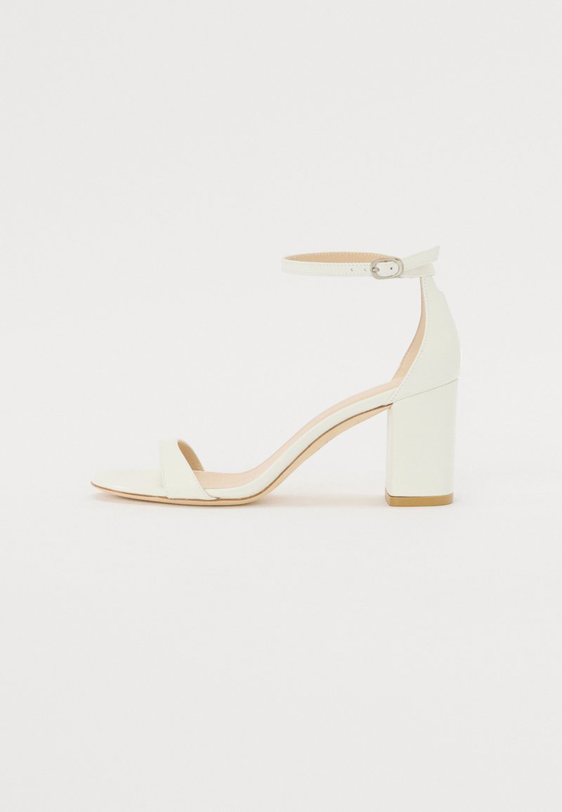 Sandale à talon bloc en cuir blanc avec une bride de cheville à boucle et un design minimaliste. Bout ouvert et textures lisses sur l'ensemble.