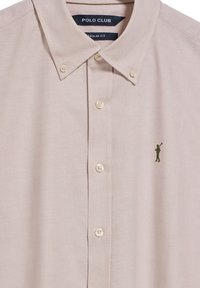 Polo shirt tan a maniche corte con colletto button-down, caratterizzato da un piccolo logo verde scuro sul lato sinistro del petto e una texture liscia. Vestibilità regolare.