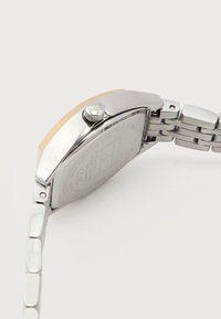 Ασημένιο μεταλλικό ρολόι χειρός με ορθογώνια κάσα και μπρασελέ με κρίκους, που δείχνει την πίσω πλευρά της κάσας με χαραγμένες λεπτομέρειες της μάρκας και του μοντέλου.