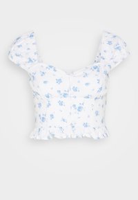 Vit kort blus med blå blommönster, puffärmar, knäppning fram och volang i fållen mot en enkel bakgrund.