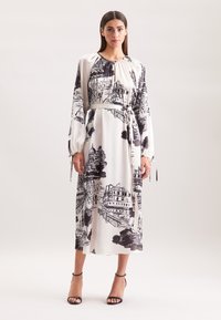 Langärmliges Kleid aus weißem Stoff mit einem schwarzen architektonischen Druck, tailliert mit einem Bindeband und mit elastischen Bündchen versehen.