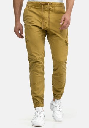 Spodnie typu cargo w kolorze musztardowej żółci, z regulowanym sznurkiem w talii, elastycznymi ściągaczami na końcach nogawek oraz bocznymi kieszeniami, wykonane z gładkiego materiału.