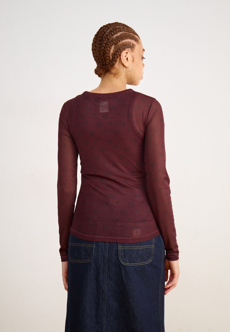 Bordeaux rode top met lange mouwen en een gladde textuur, met een subtiel patroon van zwarte cirkelvormige logo's, gecombineerd met een denim rok.