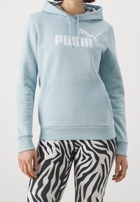 Ljusblå hoodie i mjukt tyg med en känguruficka, prydd med en vit Puma-logotyp. Matchad med leggings i svart och vitt zebramönster.