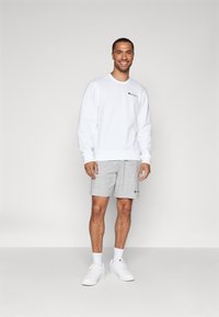 Sweat-shirt blanc avec col rond, shorts gris et baskets blanches. Présente un logo sur le sweat-shirt et les shorts. Design simple, coupe décontractée.