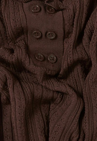 Tessuto marrone lavorato a maglia con una texture a coste, caratterizzato da una fila di quattro bottoni scuri. Il materiale appare morbido e cade delicatamente.