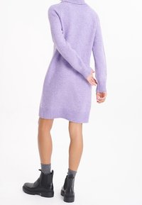 Robe en tricot lilas avec col montant, poignets et ourlet côtelés. Associée à des bottines noires et des chaussettes grises. Texture lisse, coupe ajustée.