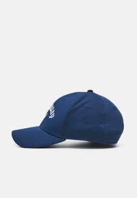 Navy blue cap with a textured mesh fabric, curved brim, and white embroidered logo on the front. Features six ventilation eyelets.