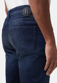 Dunkelblaue Denim-Jeans mit enger Passform, ausgestattet mit einem Lederlogo-Patch am Bund und auffälligen Nähten an den Gesäßtaschen.
