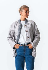 Kantet grå jakke med rund hals, knaplukning og lange ærmer. Sammen med en hvid t-shirt og blå højtaljede jeans.