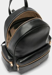 Sort læderrygsæk med rundet top, to lynlåsrum, guldfarvet hardware og en tekstureret finish. Indersiden har et logo-mønster.