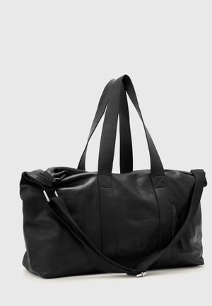 Sac polochon en cuir noir avec doubles poignées et bandoulière réglable sur un fond uni clair.