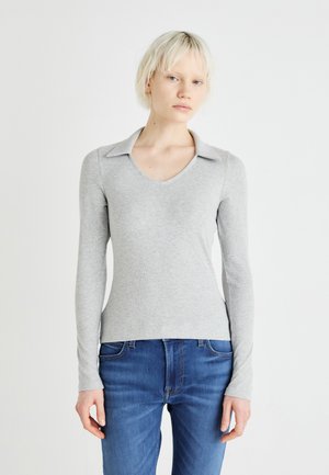 Graues langärmliges Oberteil mit V-Ausschnitt und Kragen-Design, aus einem gerippten Stoff. Getragen mit blauen Jeans, die einen figurschmeichelnden Stil zeigen.