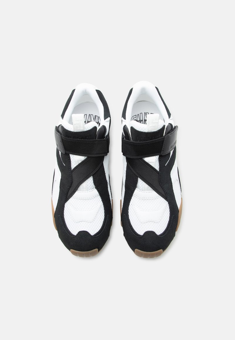 Coppia di scarpe da ginnastica bianche e nere con cinturini a velcro e suole color gomma vista dall'alto su sfondo bianco.