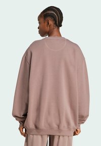 Felpa over-size di colore malva con spalle scese, orlo a coste e tessuto testurizzato. Presenta un dettaglio a cucitura circolare sul retro.