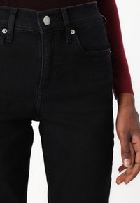 Svarta denimjeans har en hög midja, silverknappar och framfickor. Materialet verkar robust med en slät textur.
