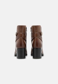 Bottes courtes en cuir marron avec un panneau arrière texturé, fermeture éclair latérale et talon bloc. Dispose d'une sangle décorative avec un accent doré.