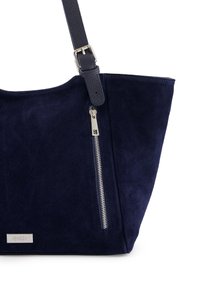 Marineblauwe suede totebag met een zilveren ritsaccent, voorzien van een gestructureerde donkerblauwe leren schouderband. Inclusief een klein metallic logoplaatje.