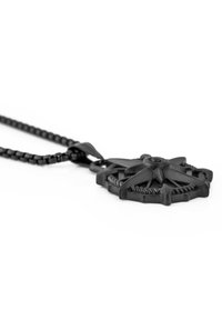 Collier pendentif noir présentant un design d'étoile détaillé et texturé, attaché à une chaîne en perles, arborant une finition mate lisse.