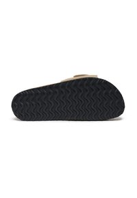 Semelle de chaussure présentant un design en caoutchouc noir texturé ondulé. La tige est en daim beige avec une fermeture à crochets et à boucle pour un enfilage facile.