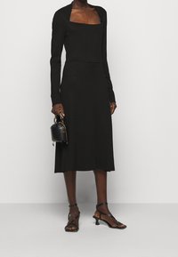 Černé šaty s jemným žebrováním, čtvercovým výstřihem a dlouhými rukávy. Kombinované s černými sandály na tenkých páscích a malou černou kabelkou.