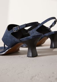 Sandales à talons en daim bleu marine avec bride à la cheville et boucle, design à bout ouvert, et talon noir épais légèrement courbé.