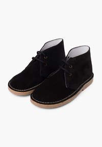 Botas de tobillo de ante negro con cordones en el frente, punta redonda y suela de goma beige. Presentan costuras alrededor de los bordes y un forro de cuero suave.