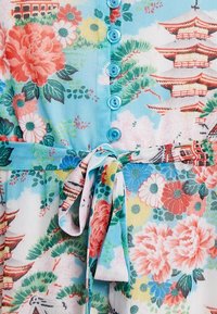 Blomstrig mönsterklänning med ljusblå bakgrund, prydd med rosa och gröna blommor, ett knytmidja och knapplås i en livfull design.