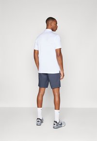 Hvit poloskjorte med korte ermer, grå shorts, hvite sokker og grå joggesko. Poloskjorten har krage og sidelufter.