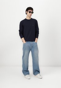 Navy sweatshirt with long sleeves, light blue wide-leg jeans, and white sneakers. Accessorized with black sunglasses.