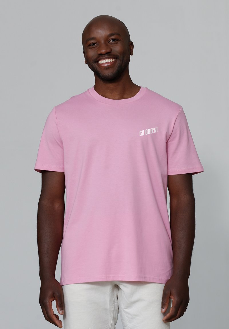 Roze katoenen t-shirt met korte mouwen, een ronde halslijn en witte "GA GROEN!" tekst op de linkerborst. Gladde textuur.