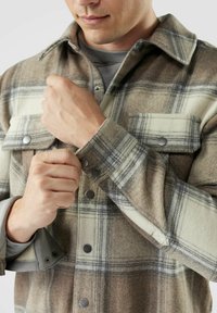 Brun och gräddfärgad rutig flanellskjorta med tryckknappar och bröstfickor; har en mjuk textur och kontrasterande tyg under ärmarna.