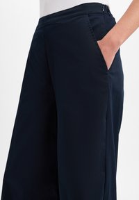 Marineblauwe wijde broek gemaakt van lichtgewicht stof, met zijzakken, een zachte textuur en een nette snit met een ritssluiting.