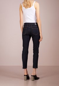 Tmavě modré džíny s úzkým střihem, středním pasem a dvěma zadními kapsami. Spárovány s bílým tílkem a černými lodičkami na podpatku.