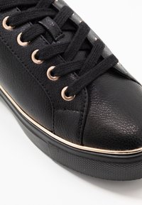 Svart lädersneaker med texturerad ovandel, rund tå, guldöglor och gummisula med kontrasterande guldtrim.