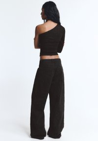 Črn enoročni top z rahlim bleščanjem, kombiniran z ohlapnimi črnimi hlačami z teksturiranimi vzorci in žepi.