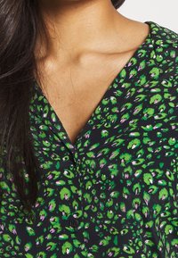 Green and purple floral patterned blouse with a V-neck, short sleeves, and black background, made from lightweight fabric. Button detail visible.