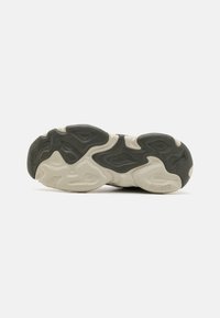 Semelle de sneaker avec un design ondulé. Dessus en caoutchouc vert foncé avec des accents texturés, semelle intermédiaire de couleur crème et détail de logo en relief.