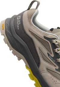 Beige und graue Wanderschuhe mit einer strukturierten Oberfläche und haltbarem Mesh. Sie verfügen über eine robuste Sohle, eine Schnürung und einen auffälligen gelben Akzent.