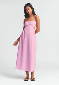 Vaaleanpunainen maksimekko ohuilla olkaimilla, jossa on neliömainen pääntie ja sivuleikkaukset. Kangas näyttää kevyeltä ja sileältä.