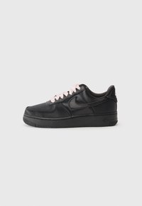 Fekete sneaker sima bőr külsővel, kontrasztos rózsaszín fűzőkkel, lapos gumitalppal és dombornyomott logóval a sarkán.