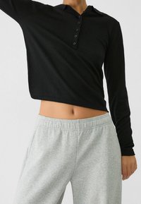 Czarna longsleeve henley z guziczkami, zestawiona z jasnoszarymi spodniami dresowymi. Materiał wydaje się miękki i ma luźny krój.