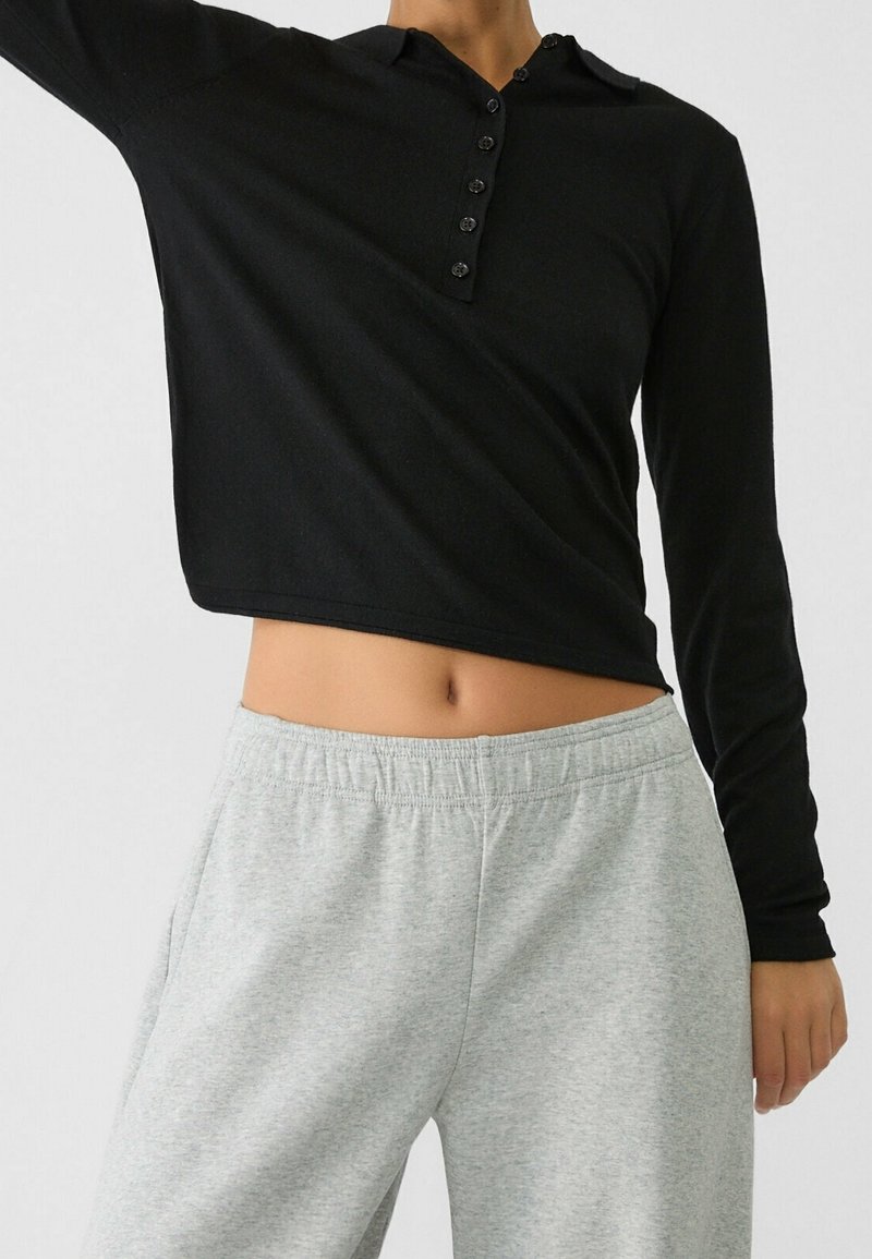 Czarna longsleeve henley z guziczkami, zestawiona z jasnoszarymi spodniami dresowymi. Materiał wydaje się miękki i ma luźny krój.
