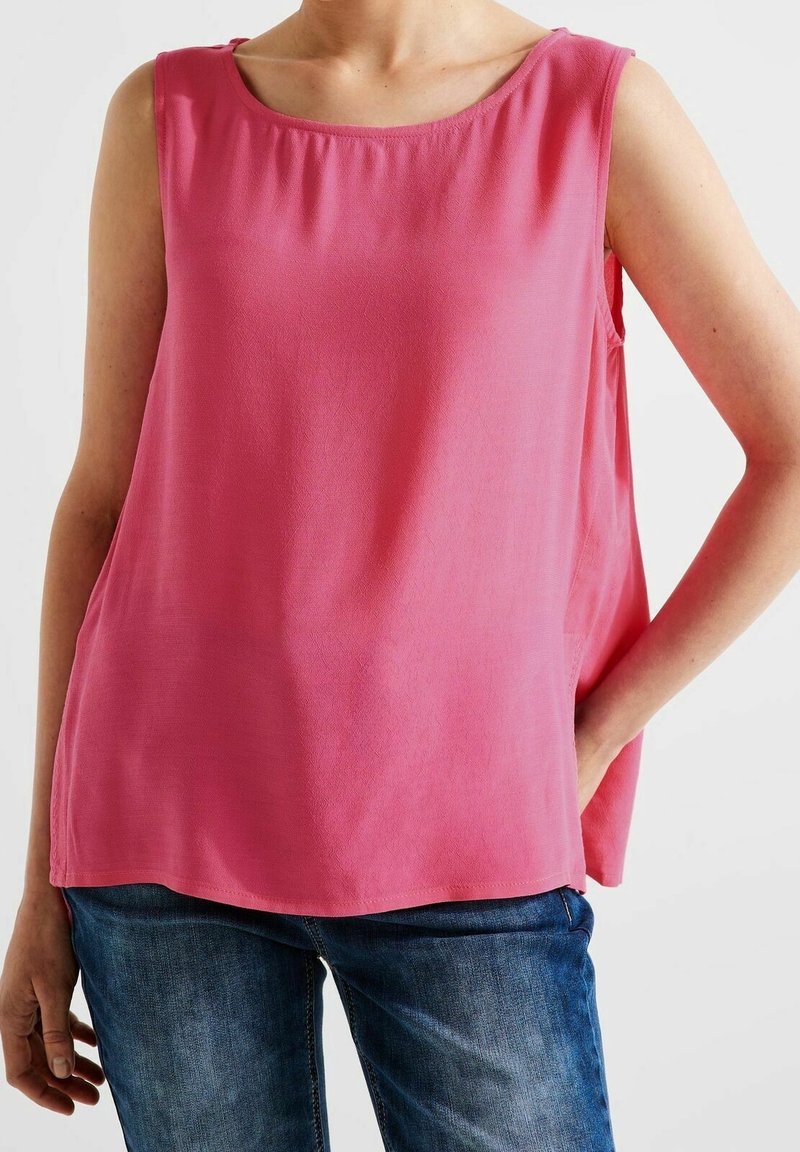 Ärmlös topp i klar rosa, med rund halsringning och slät textur. Matchad med blå jeans som visar en avslappnad passform.