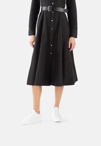 Black button-up dress with long sleeves and a fitted waist, featuring a wide skirt and a black belt. Paired with white sneakers.